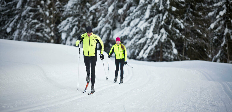 Zwei Langläufer:innen beim Langlaufen auf der Loipe Obertilliach
