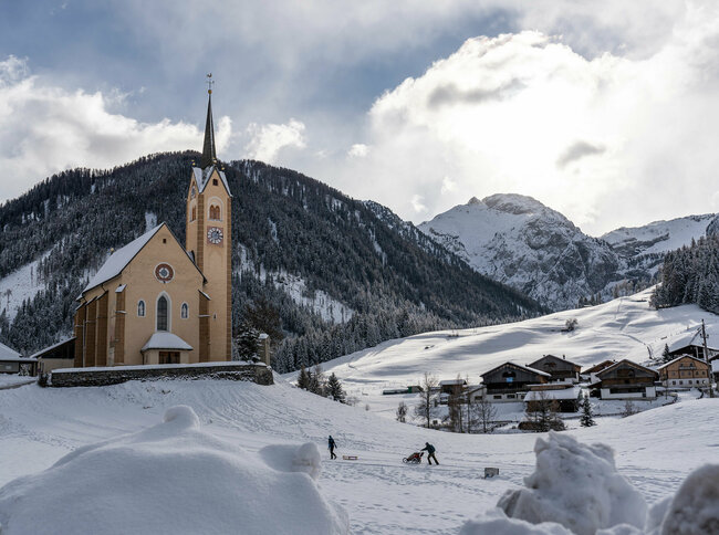 Kartitscher Pfarrkirche im Winter umgeben von schneebedeckten Feldern und den Karnischen Alpen im Hintergrund