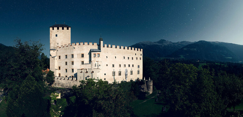 Aussenaufnahme bei Nacht von Schloss Bruck in Lienz mit Bergkulisse und Sternenhimmel im Hintergrund.