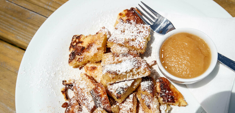 Kaiserschmarren mit Apfelmus in einem separaten Schüsselchen auf einem weißen Teller.