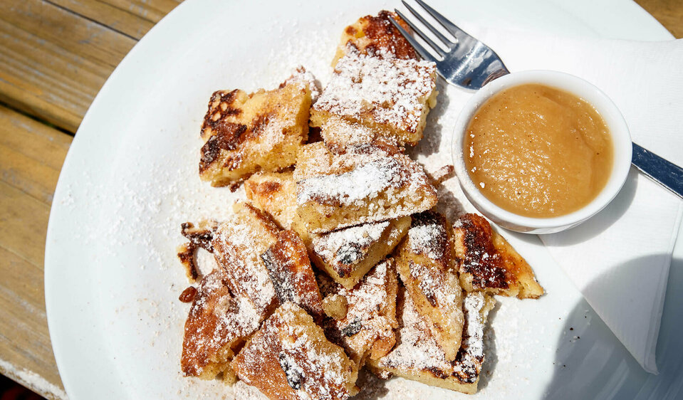Kaiserschmarren mit Apfelmus in einem separaten Schüsselchen auf einem weißen Teller.