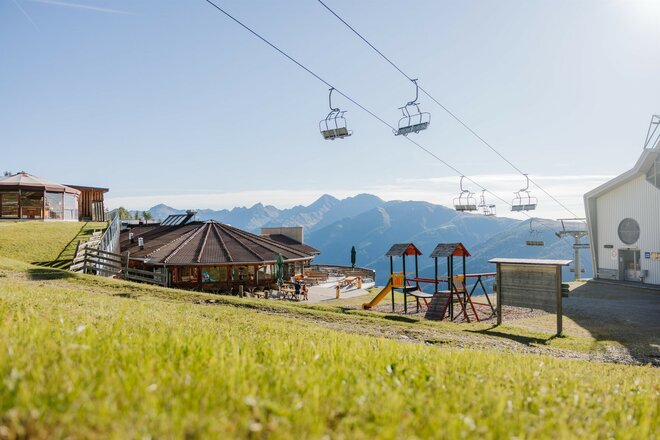 Rechts unten ist die Gondelstation und gegenüber ein Gebäude. Neben dem Gebäude ist ein Spielplatz.