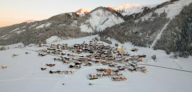 Drohnenaufnahme vom idyllischen Haufendorf Obertilliach bei romantischer Sonnenuntergangsstimmung im Winter.