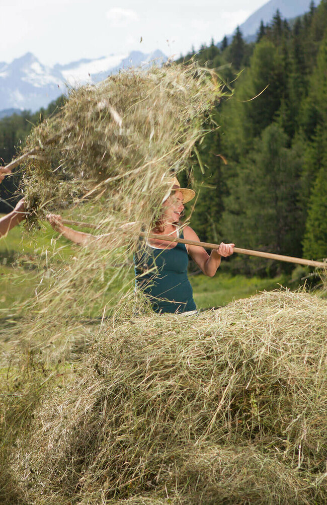 Ein Mann und eine Frau auf einer Wiese mit Heu und Heugabeln.