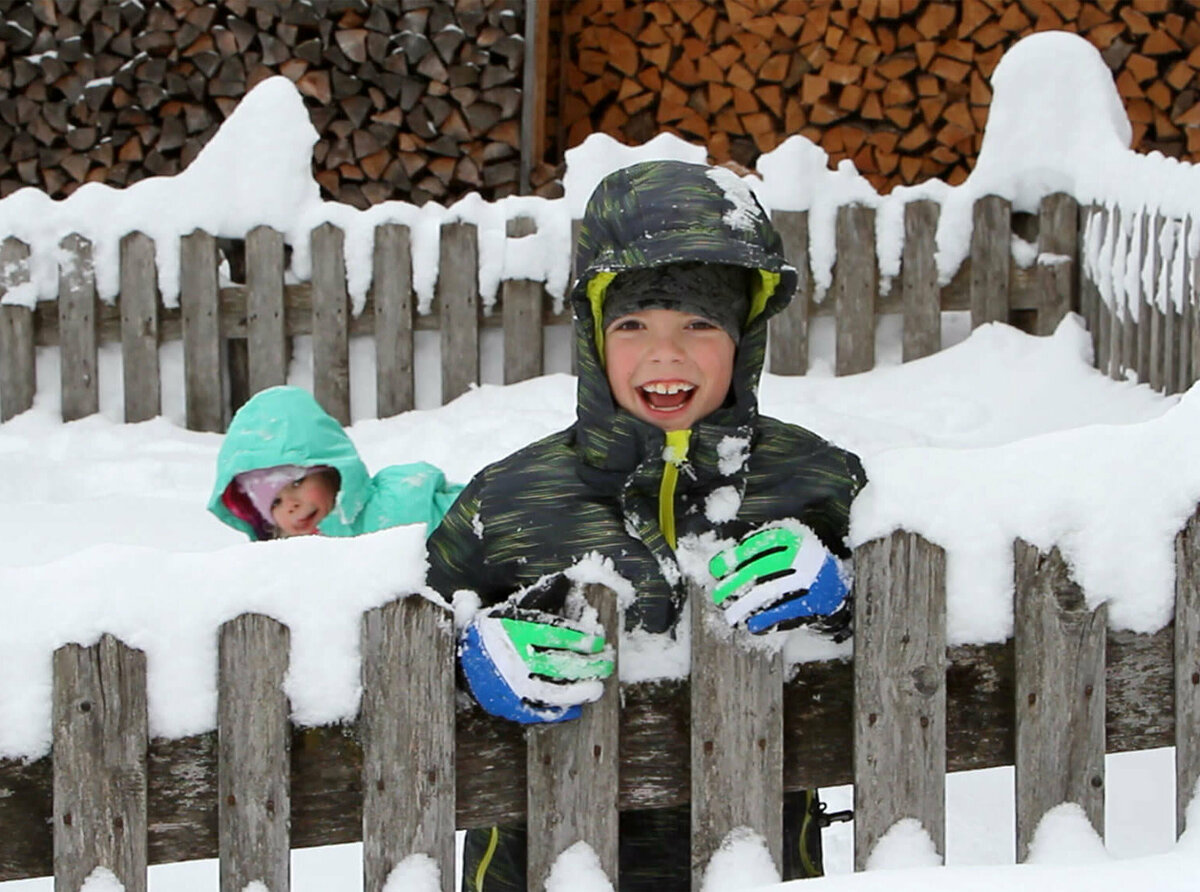 Zwei Kinder spielen bei Schneefall im frischen Pulverschnee