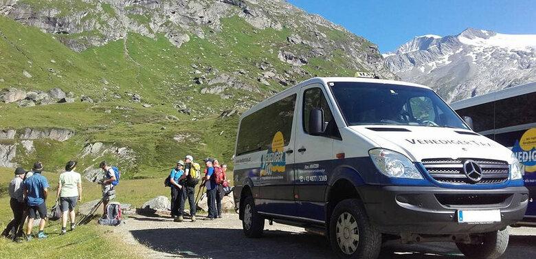 Zwei Venediger-Wandertaxis stehen auf einem Weg vor einer imposanten Bergkulisse. Dahinter stehen mehrere Wandergäste.