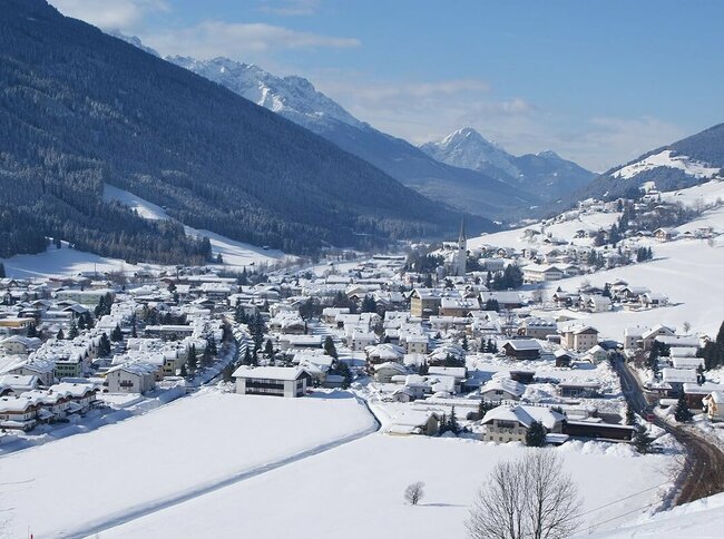 Ortsansicht von Sillian mit verschneiter Winterlandschaft und Blick auf die Sextener Dolomiten im Hintergrund.