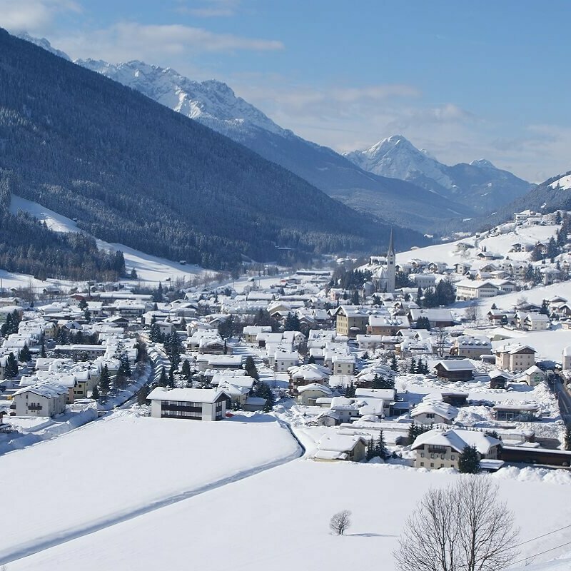 Ortsansicht von Sillian mit verschneiter Winterlandschaft und Blick auf die Sextener Dolomiten im Hintergrund.
