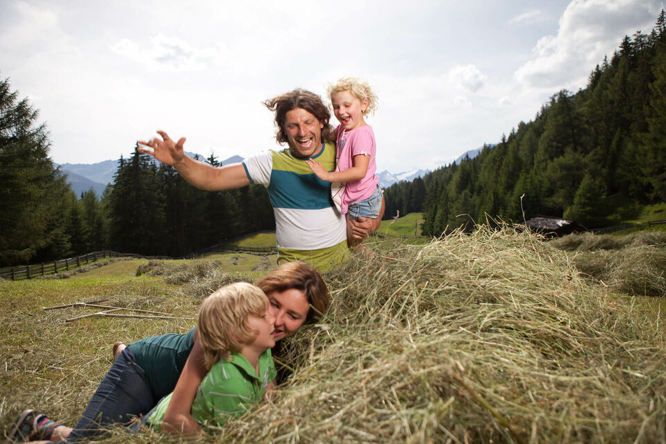 Eine Familie macht Urlaub am Bauernhof und spielt im Heu auf einer Wiese.