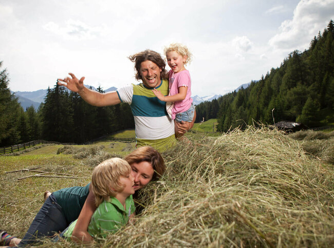 Eine Familie macht Urlaub am Bauernhof und spielt im Heu auf einer Wiese.