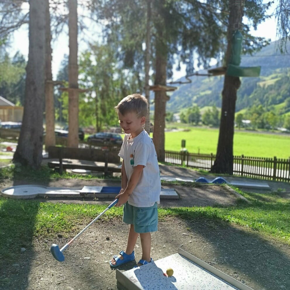 Auf dem Bild ist ein kleiner Junge im wichtelpark zu sehen, der am Minigolfplatz sein Können beweist.