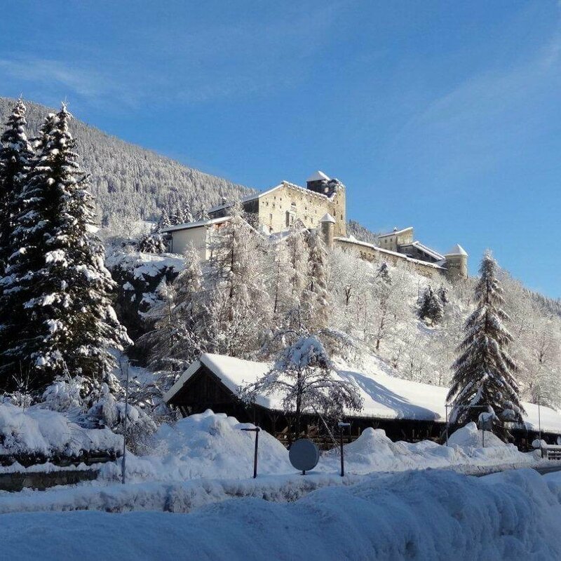 Winterliche Landschaft mit der Punbrugge im Vordergrund und der  Burg Heinfels im verschneiten Wald im Hintergrund.