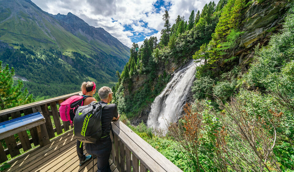 Weitwandern auf der Glocknerkrone in Osttirol, Etappe 2: Ein Wanderpaar betrachtet den Stotzbach-Wasserfall nahe dem Kalser Tauernhaus durch ein Fernglas.