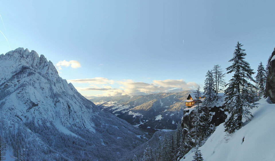 Panoramablick auf die beleuchtete Dolomitenhütte im Winter. Die Landschaft ist tief verschneit.