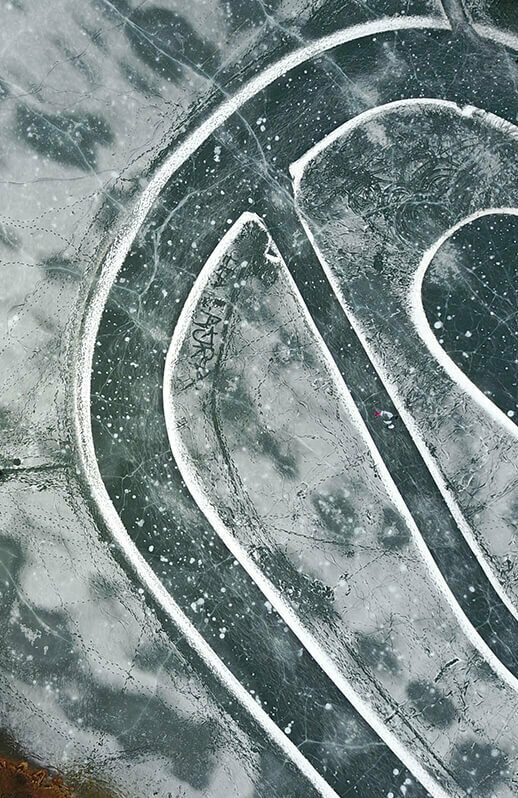 Der Eislaufplatz am Tristachersee aus der Vogelperspektive fotografiert. Eine ovale Spur ist auf dem Eis.