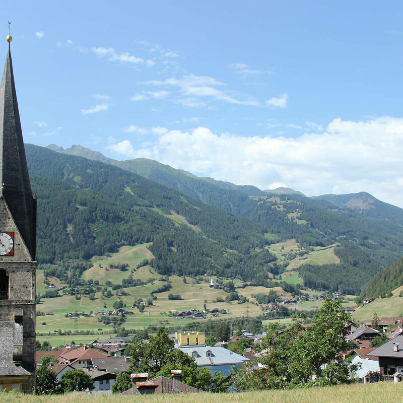Blick auf den Kirchturm und die umliegende Landschaft in Matrei, an einem sonnigen Tag.