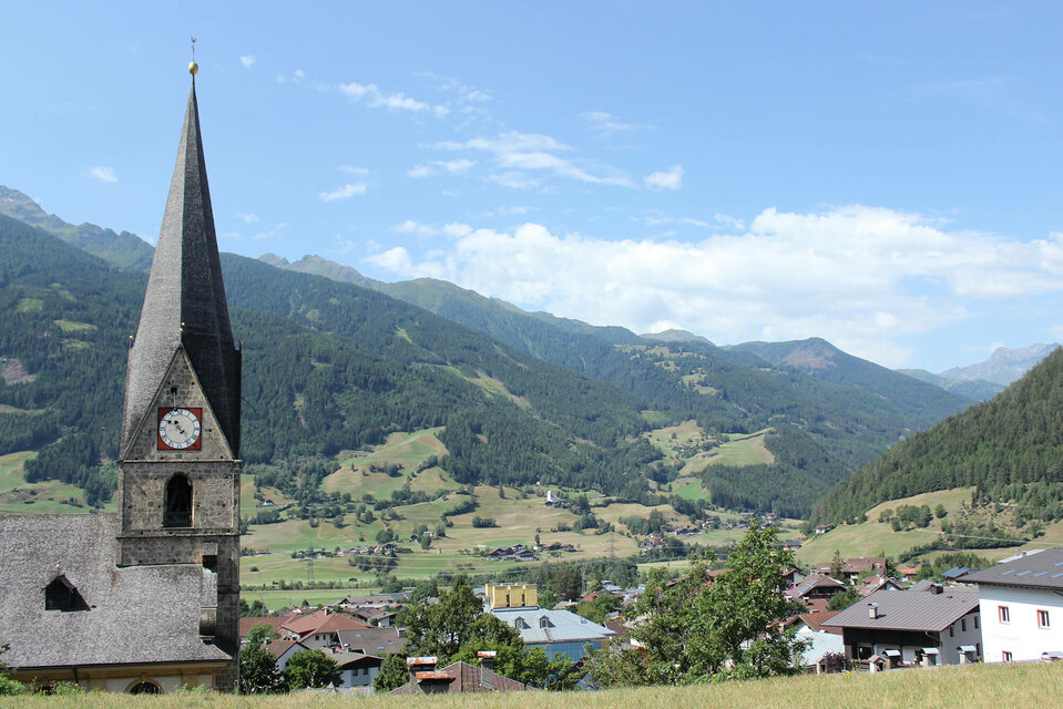 Blick auf den Kirchturm und die umliegende Landschaft in Matrei, an einem sonnigen Tag.