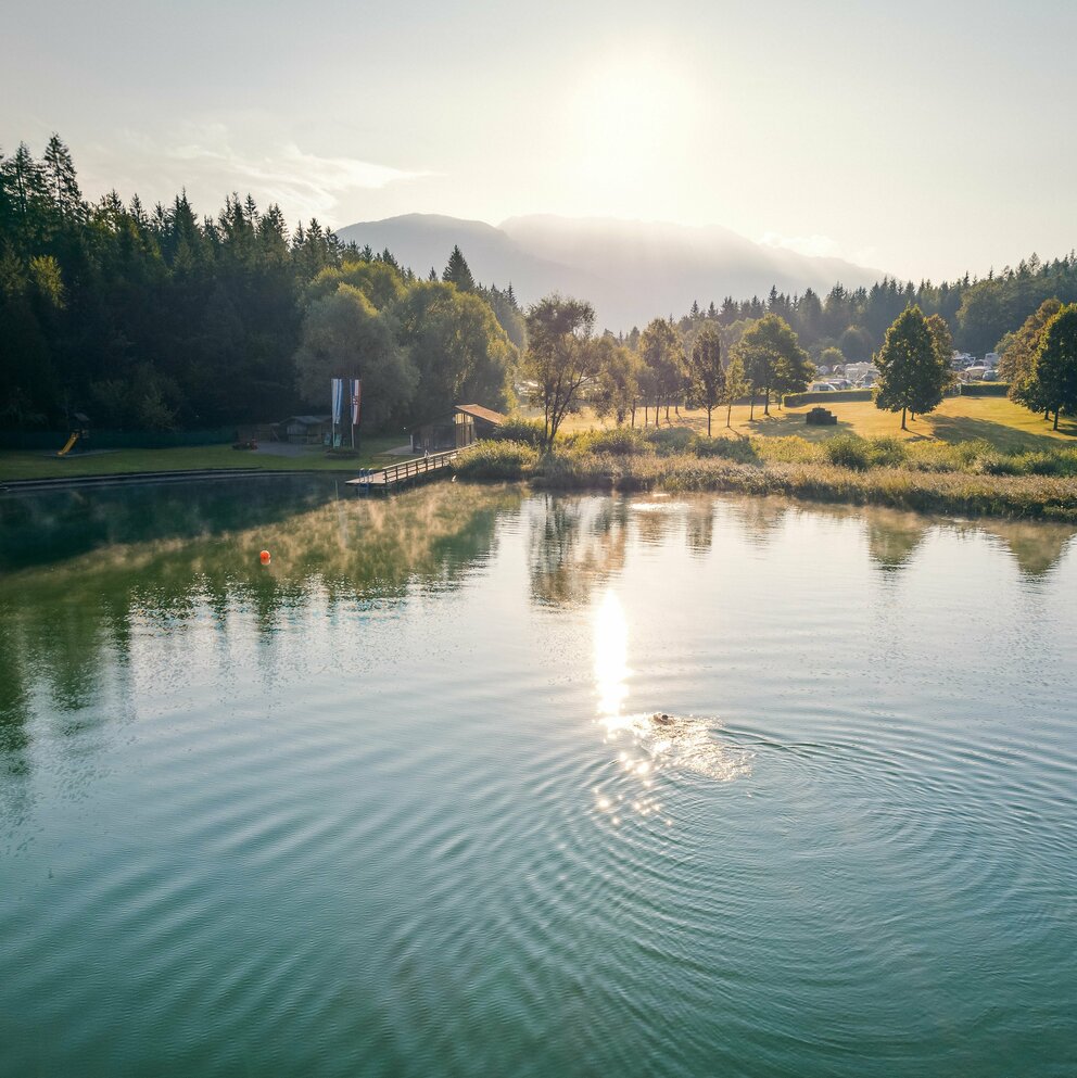 Eine Person schwimmt in der Morgensonne durch den menschenleeren Tristacher See.