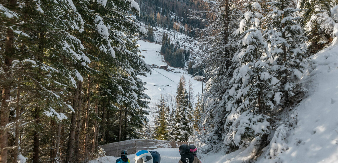 Eine Familie in Skianzügen rodelt auf ihren Schlitten talwärts auf der Rodelbahn im Winkeltal in Außervillgraten, Osttirol.