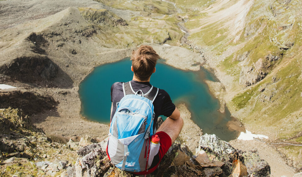 Ein wanderer Sitzt auf ein paar Felsen über dem türkisen Eissee inmitten der Bergwelt von Prägraten.