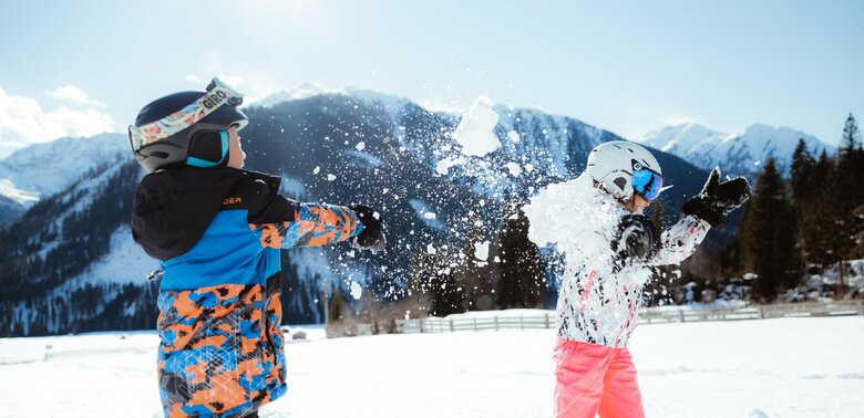 Zwei Kinder machen eine lustige Schneeballschlacht im Kinderland in Obertilliach bei strahlend schönem Wetter.