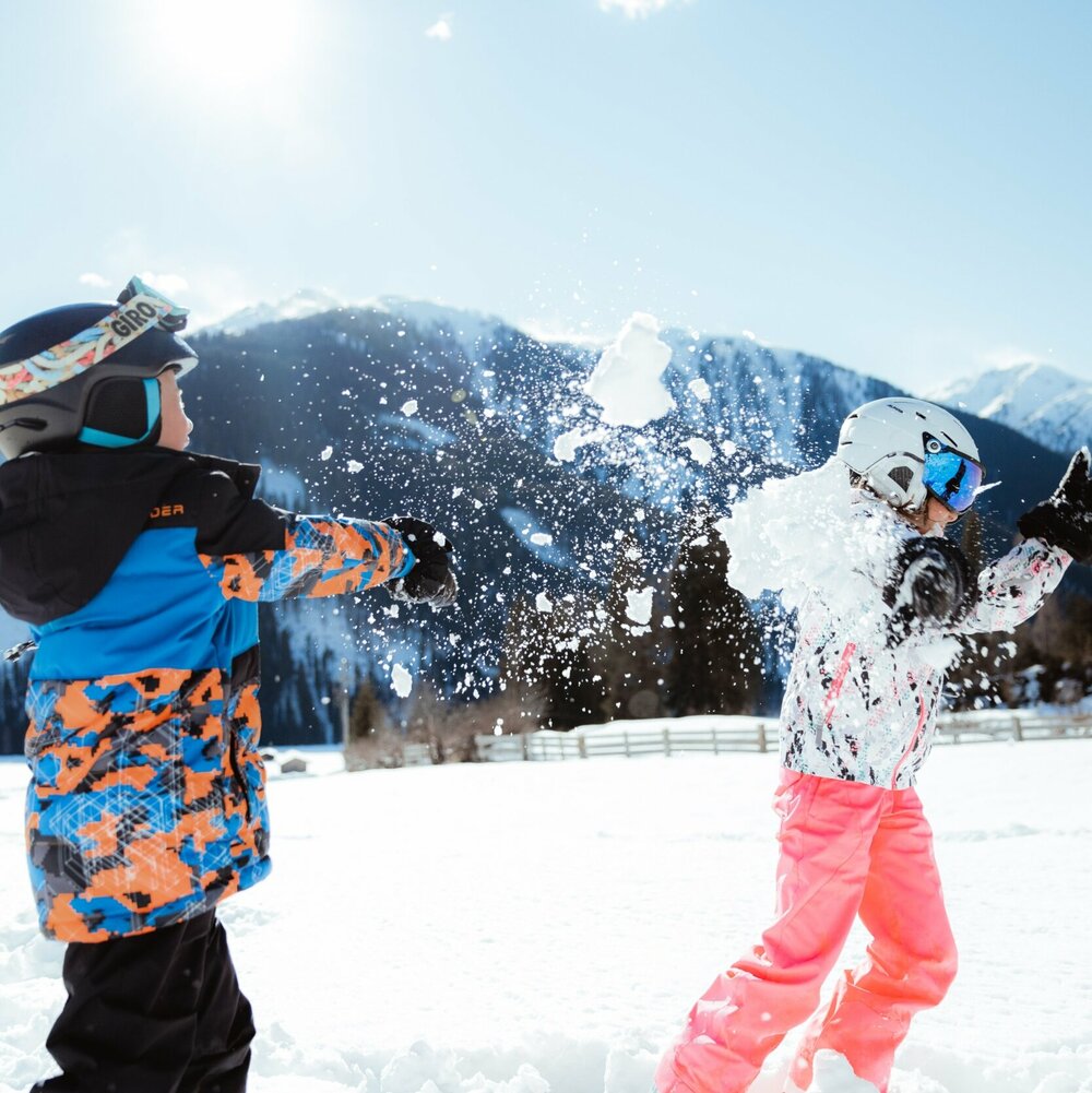 Zwei Kinder machen eine lustige Schneeballschlacht im Kinderland in Obertilliach bei strahlend schönem Wetter.