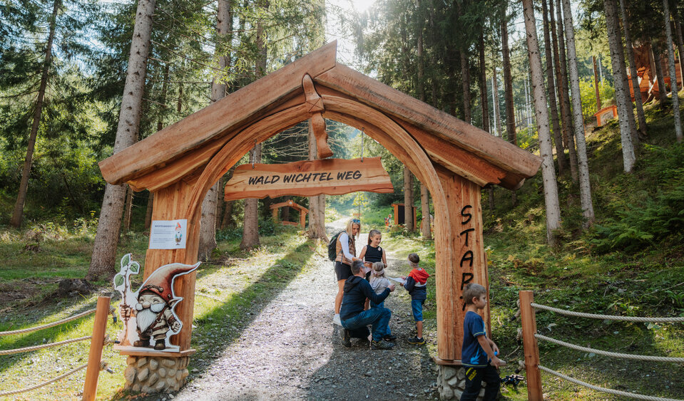 Das Bild zeigt eine Familie am hölzernen Eingangsportal zum Waldwichtelweg.