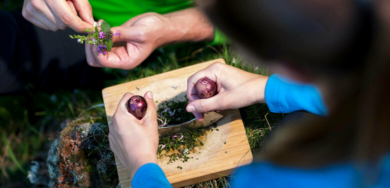 Kräuter werden auf einem Schneidebrett aus Holz mit einem Wiegemesser fein gehackt.