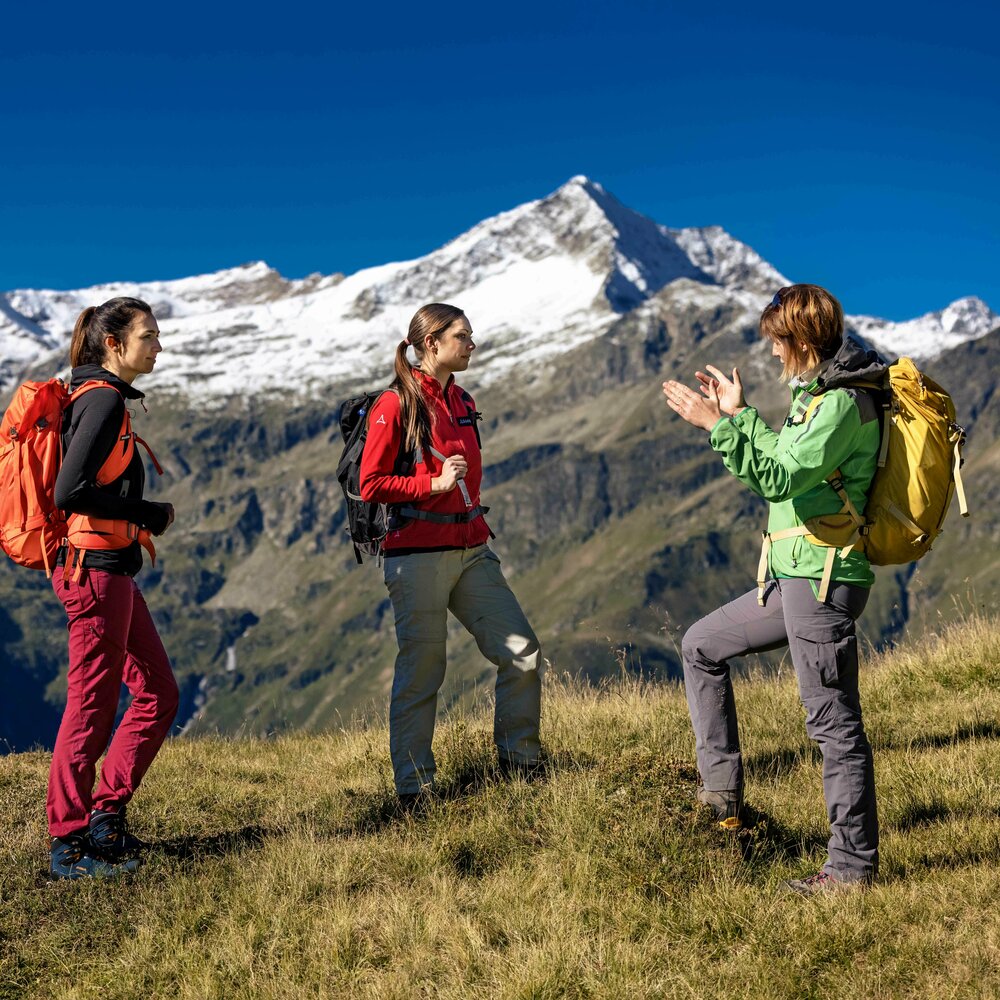 Eine Rangerin zeigt zwei Frauen die Nationalparkregion bei einer Rangerwanderung mit Wildspitze im Hintergrund.
