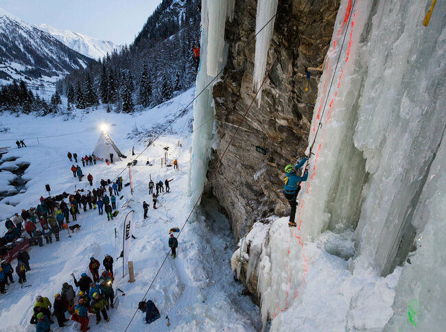 Viele Teilnehmer beobachten vom Boden aus einzelne beim Eisklettern über die steilen eisbedeckten Felswände.