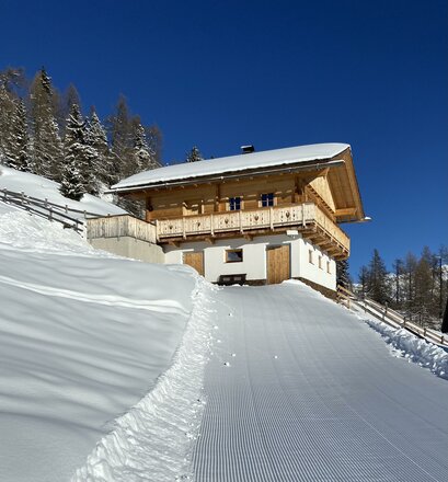 Ein chalet in den Bergen, umgeben von schneebedeckten Bäumen. Der klare blaue Himmel rundet die Winterlandschaft ab.