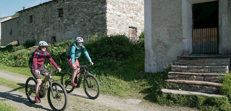 Zwei Radfahrer fahren auf einem Schotterweg vorbei an den Jagdhausalmen.