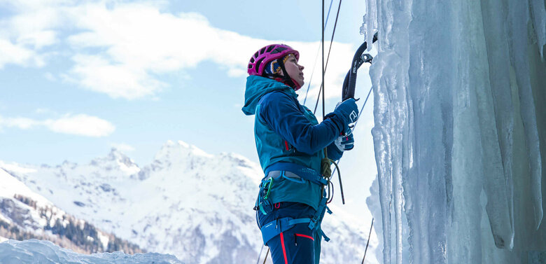 Eine Person steht am Start einer abenteuerlichen Kletterroute über einen zugefrorenen Wasserfall.