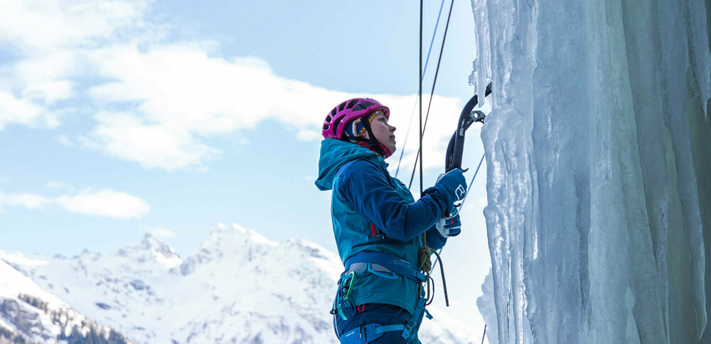 Eine Person steht am Start einer abenteuerlichen Kletterroute über einen zugefrorenen Wasserfall.