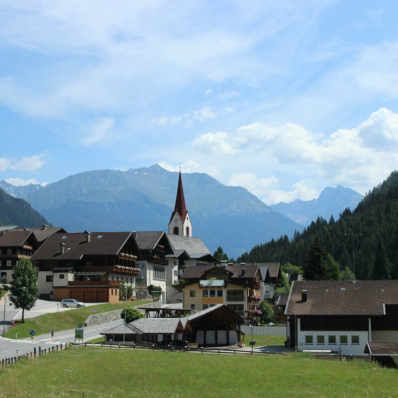 Hopfgarten i. D. im Sommer mit der Kirche und den Bergen im Hintergrund.