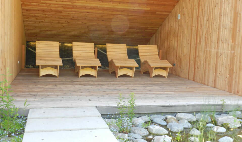 Vier Sommerliegen aus Zirbenholz stehen unter einem Vordach