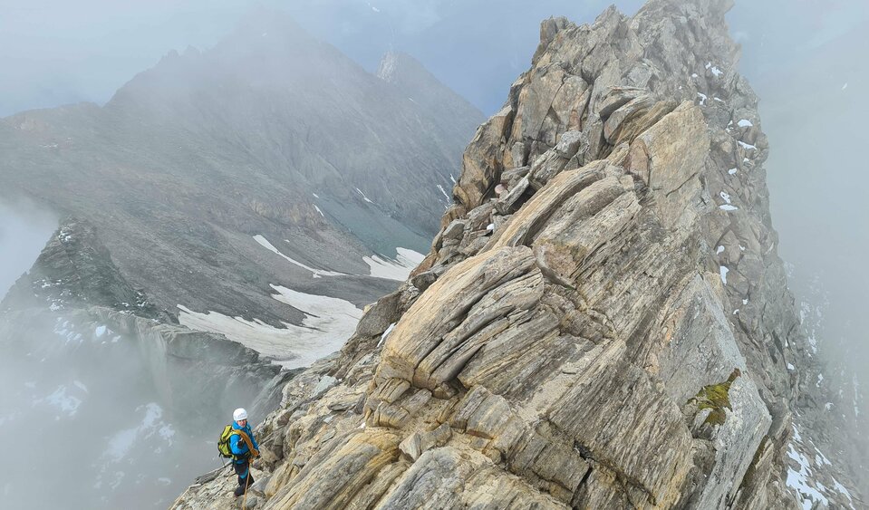 Ein Bergsteiger mit voller Ausrüstung steht auf dem Gipfel des Hohen Eichham umringt von Nebelschwaden.