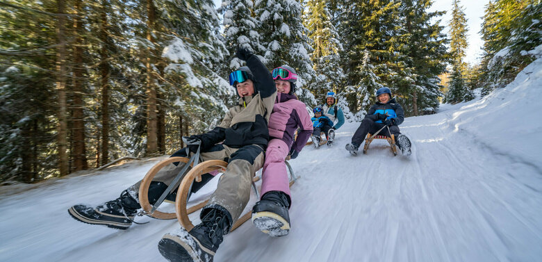 Eine fünfköpfige Familie in bunten Skianzügen auf der rasanten Rodelabfahrt in Außervillgraten.