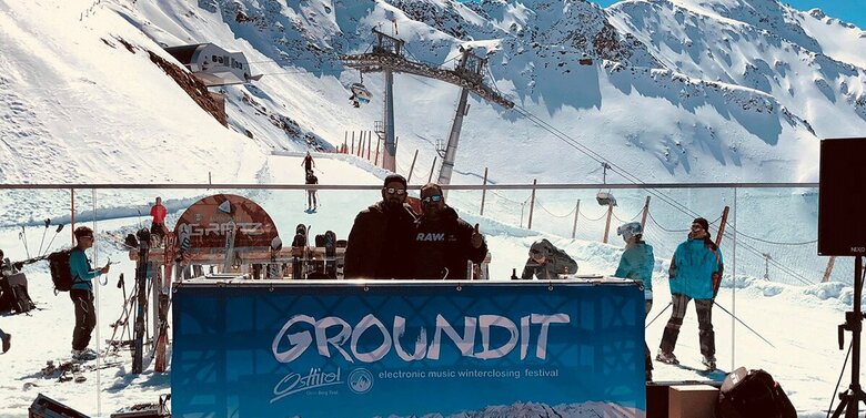 Zwei Erwachsene hinter einer Art Theke beim Ground it Festival auf einer Sonnenterrasse in einem Skigebiet.