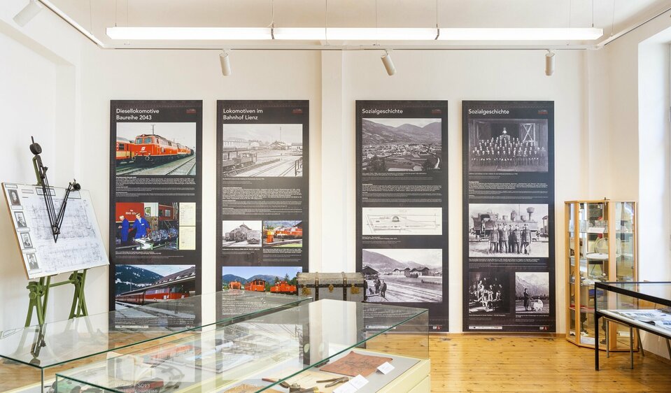 Im Ausstellungsraum des Eisenbahnmuseums in Lienz sind an der Wand beeindruckende Fotos von historischen Loks aus vergangenen Zeiten zu sehen.