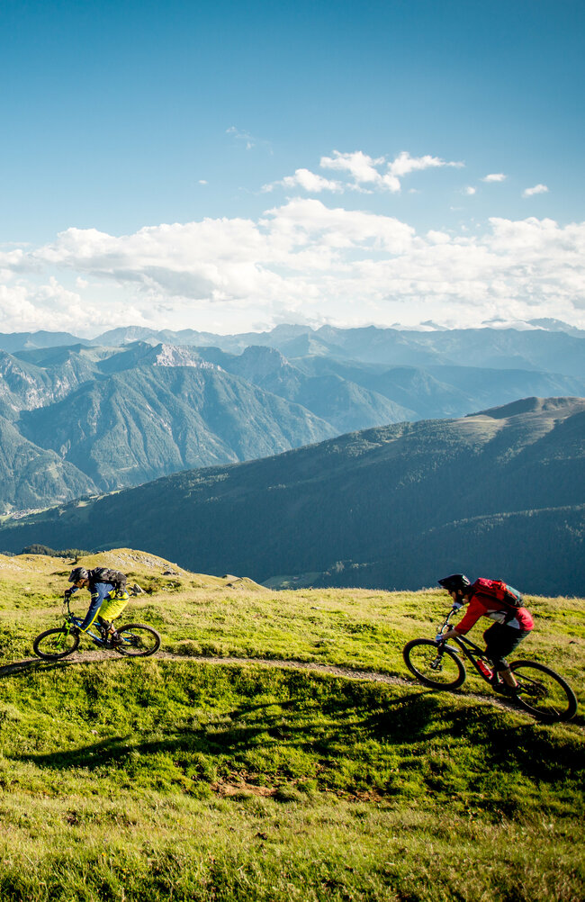 Zwei Radfahrer auf einem schmalen Trail mit einzigartigem Bergpanorama.