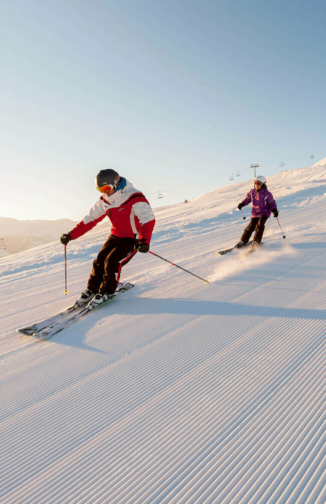 Ein Skilehrer fährt mit mehreren Kindern über eine frisch präparierte Abfahrt im Skigebiet Zettersfeld.