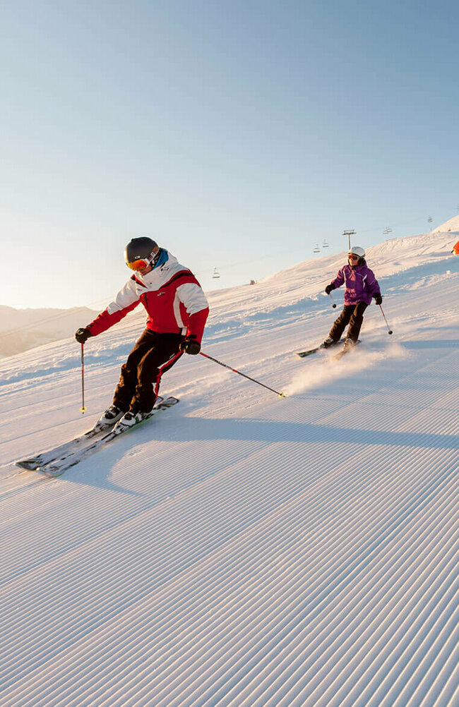 Ein Skilehrer fährt mit mehreren Kindern über eine frisch präparierte Abfahrt im Skigebiet Zettersfeld.