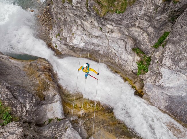 Eine Frau mit gelber Jacke geht über eine luftige Seilbrücke über den Fluss in der Galitzenklamm.
