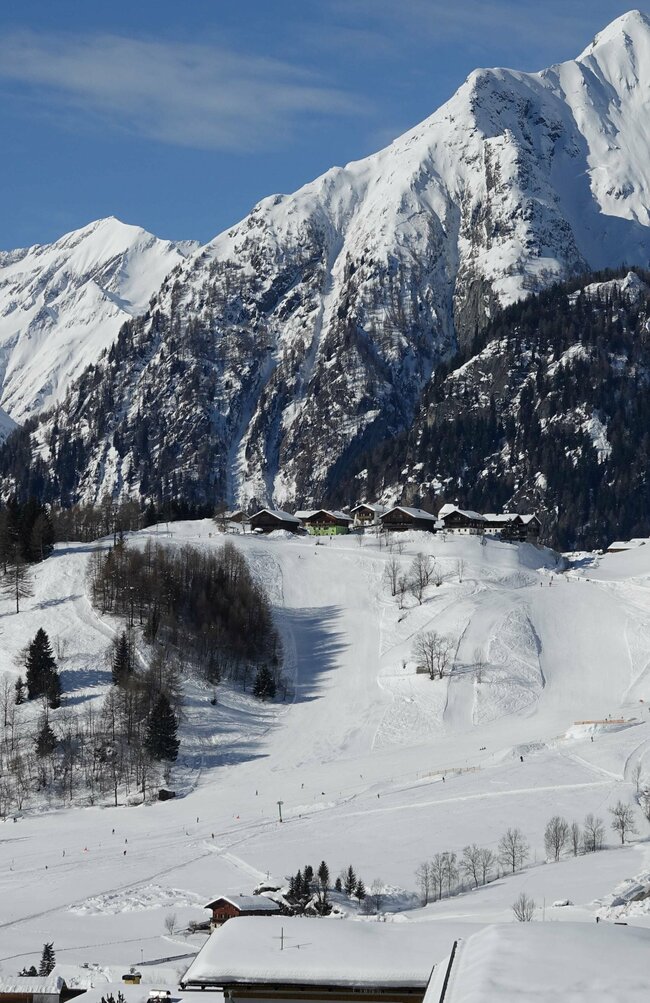 Blick von oben auf das Familienskigebiet Prägraten am Großvenediger mit schneebedeckter Bergkulisse im Hintergrund.