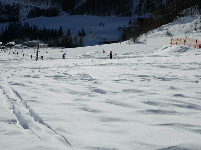 Blick auf ein Schneefeld vor dem Bichllift Schlepper. Im Lift fahren mehrere Personen. Dahinter ist eine Slalomstrecke aufgebaut.