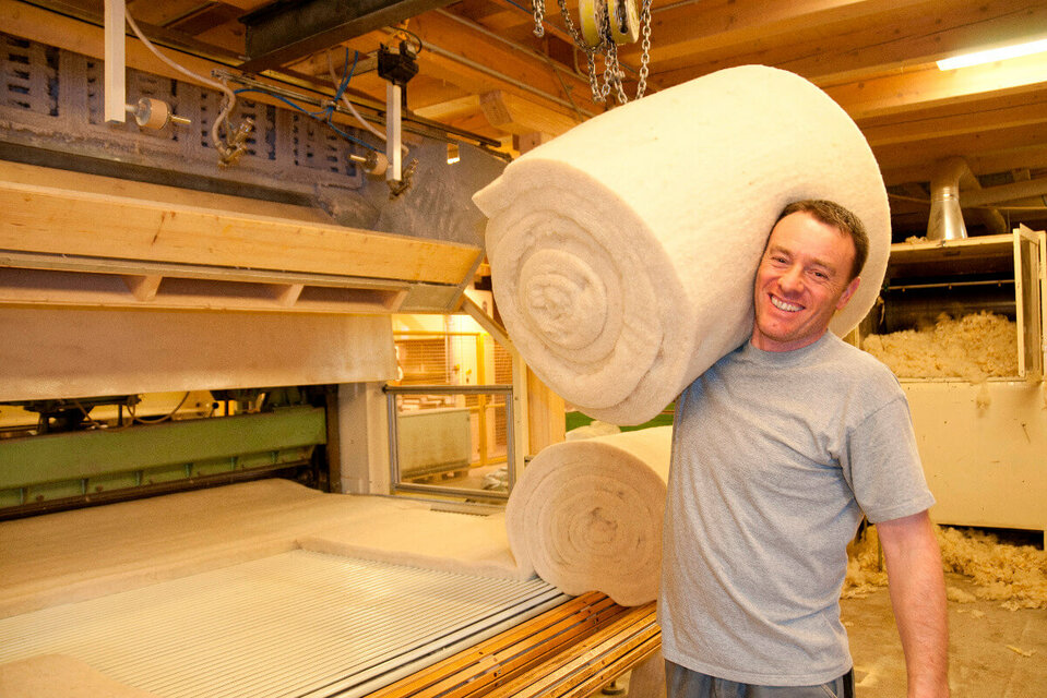 Ein männlichter Mitarbeiter trägt einen Ballen Schafwolle auf seiner Schulter