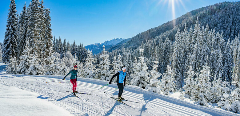 Zwei Langläufer:innen genießen das Panorama der verschneiten Landschaft um die Langlaufloipe in Obertilliach.