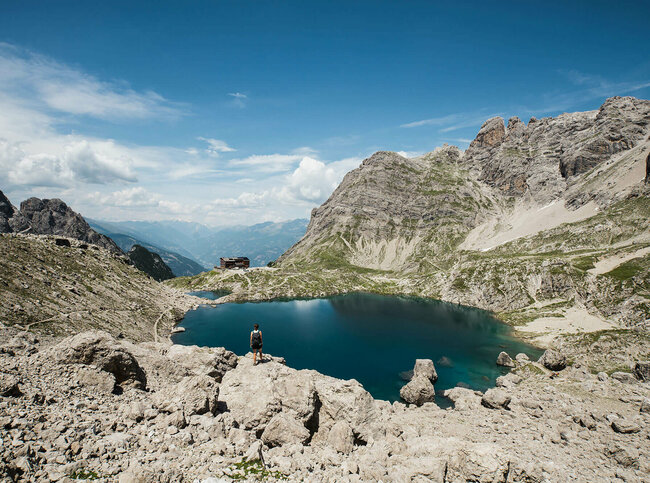 Eine Frau steht auf einem Felsbrocken vor dem Laserzsee und der Karlsbader Hütte in den Lienzer Dolomiten.