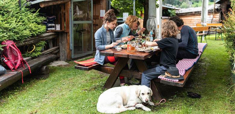 Familie macht mit ihren Hund bei einer Buschenschenke Rast und konsumieren verschiedene Getränke und Speisen.